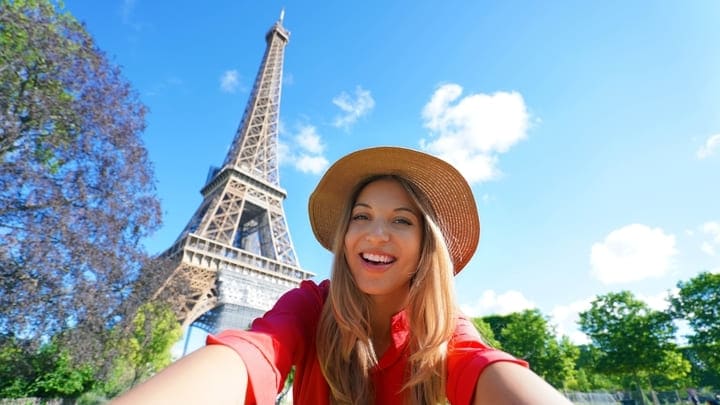Woman taking a selfie in front of the Eiffel Tower on a summer day