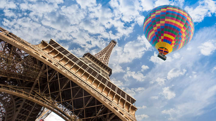 View looking up from the base of the Eiffel Tower, with a hot air balloon overhead